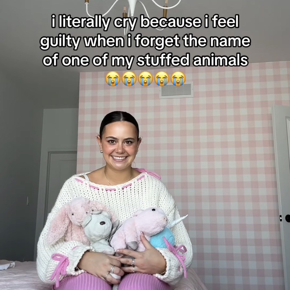 Screenshot from one of Spencer's TikTok videos showing her sitting on her bed with a fake smile holding various stuffed animals and a caption reading "i literally cry because i feel guilty when i forget the name of one of my stuffed animals".